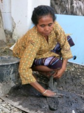 Crouching on the stony ground, a woman rubs black dye made from mud and buffalo dung into a skein of cotton.