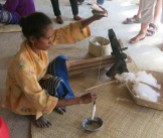 After gently rolling it into a cocoon shape, the woman spins the cotton by hand, pivoting a wooden spindle on a saucer.