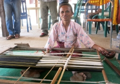 Using a half-coconut shell, a weaver threads cotton onto a loom in the colour combinations required for a particular tais pattern.