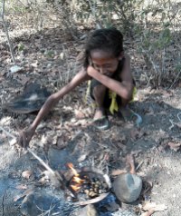 A shy young girl roasts freshly-picked cashews over an open fire on the beach at Suai-Loro.